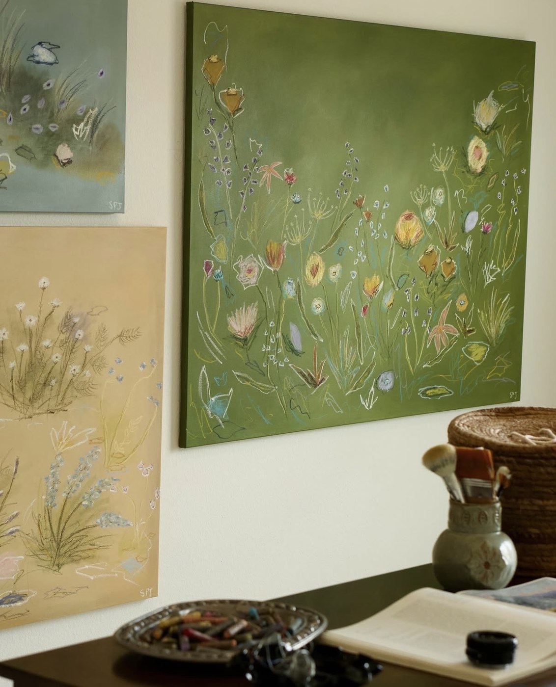 A large green wildflower canvas on the studio wall beside two smaller pieces